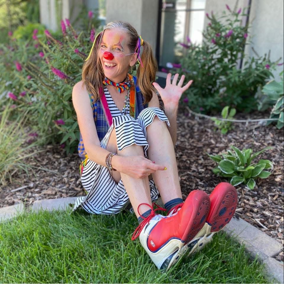 A smiling clown sitting outside in oversized red shoes